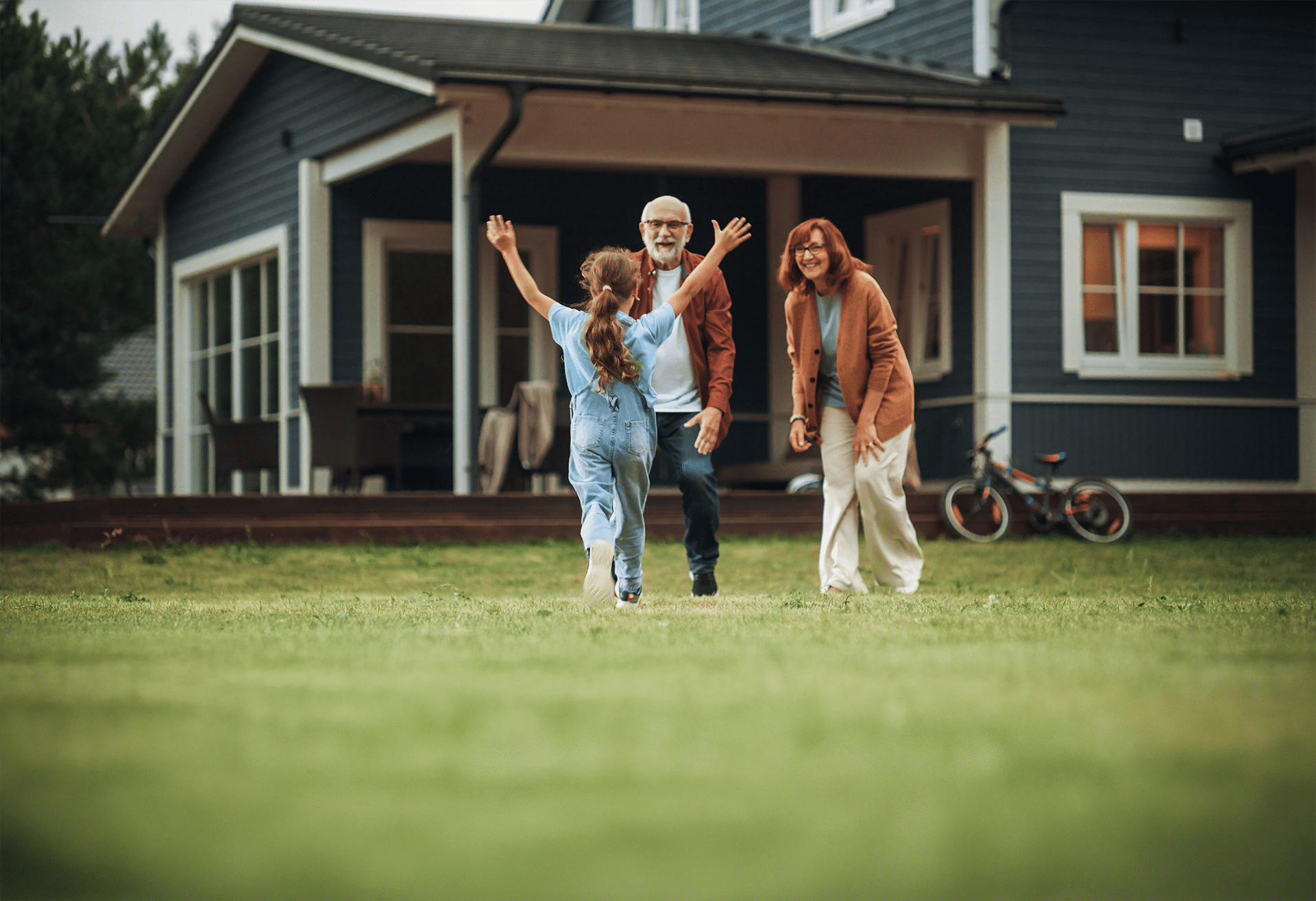 Young girl running through yard toward two older people
